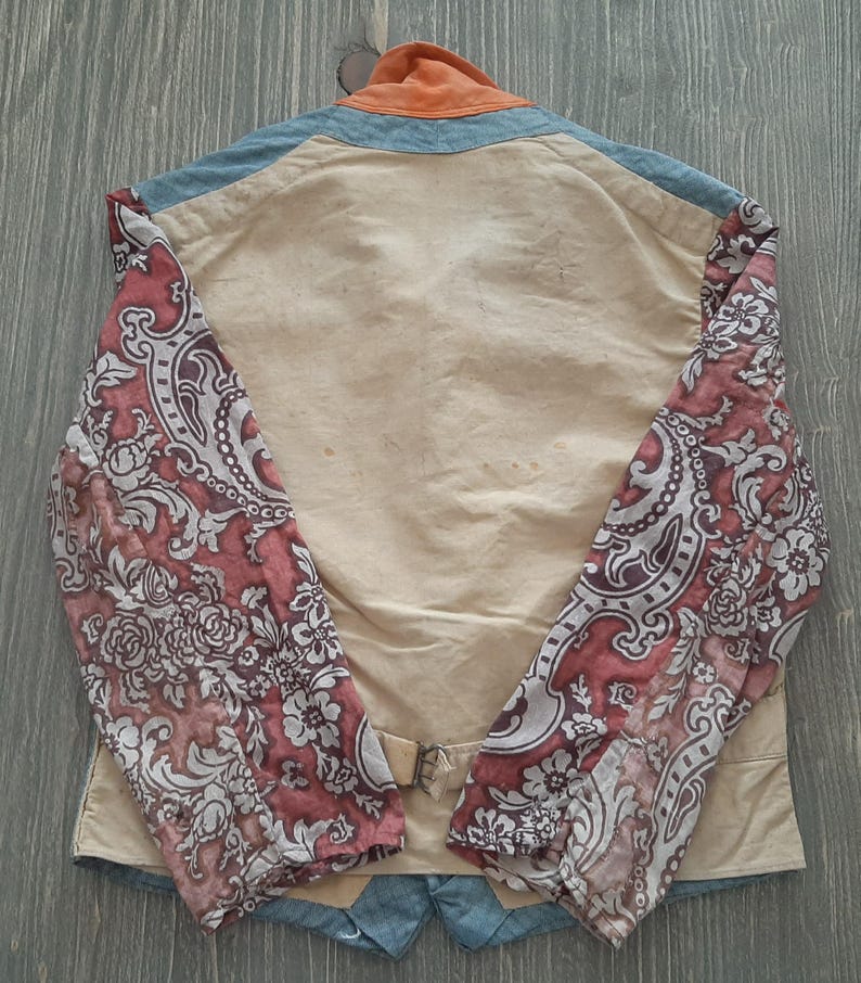 May include: A beige jacket with a floral pattern on the sleeves. The jacket has a blue denim collar and a orange collar lining. The jacket has a buckle closure at the waist.