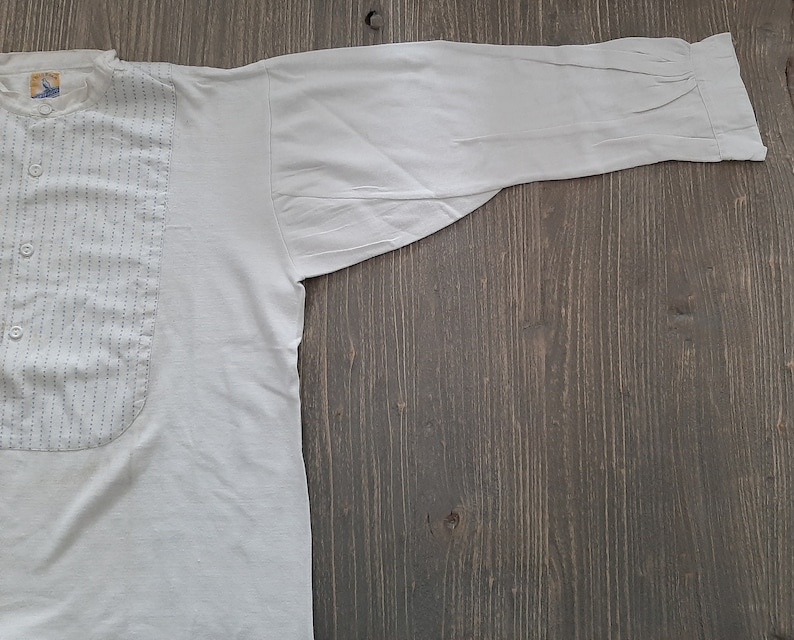 Op de afbeelding: Een wit overhemd met lange mouwen, een knoopsluiting en een decoratief paneel aan de voorkant. Het paneel heeft verticale stiksels.