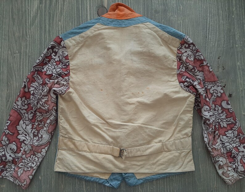 May include: A cream-colored jacket with a blue collar and cuffs. The sleeves are made of a red and white floral fabric. The jacket has a belt and a single button closure.