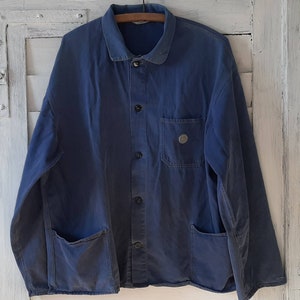 May include: A dark blue work jacket with a button-up front, two large pockets on the bottom, and a smaller pocket on the chest. The jacket has a collar and long sleeves.