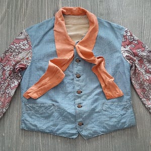May include: A blue denim jacket with a peach-colored scarf tied around the neck. The sleeves are made of a patterned fabric with pink and white floral designs.