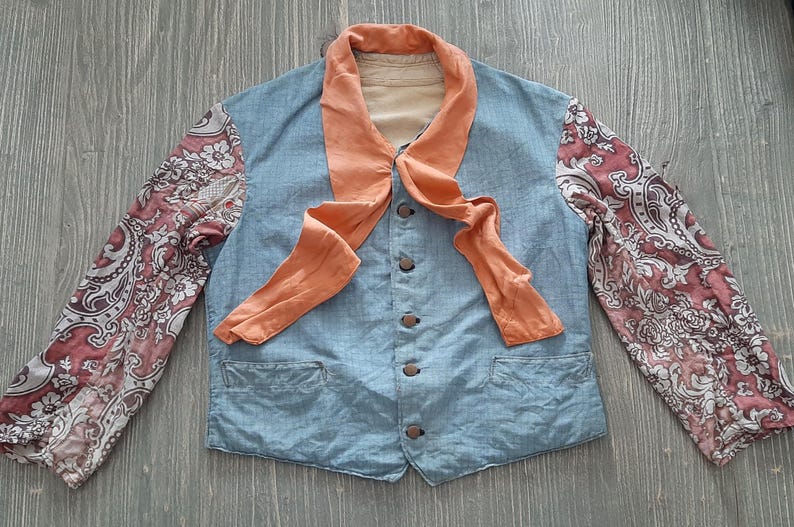 May include: A blue denim jacket with a peach-colored scarf tied around the neck. The sleeves are made of a patterned fabric with pink and white floral designs.
