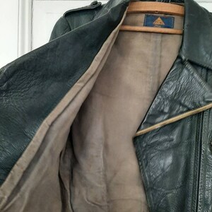 May include: A dark green leather jacket with a zipper closure and a brown lining. The jacket has a label on the inside that says "212".