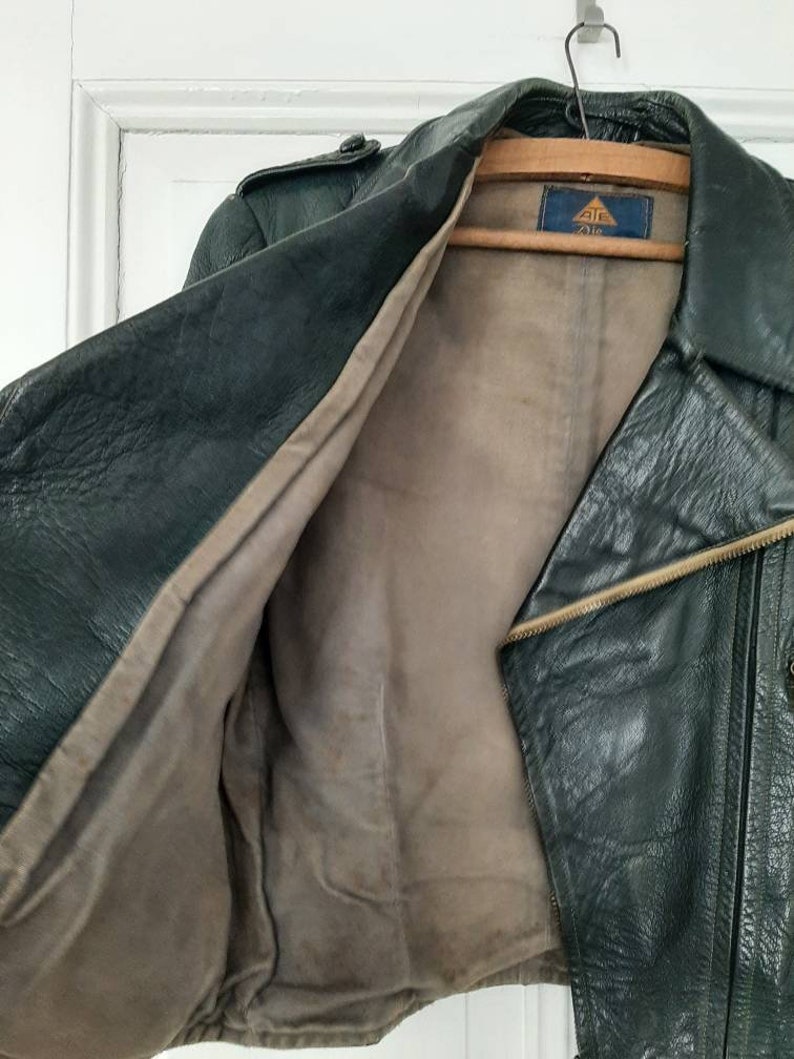 May include: A dark green leather jacket with a zipper closure and a brown lining. The jacket has a label on the inside that says "212".