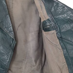 May include: A dark green leather jacket with a brown lining. The jacket is unbuttoned and the lining is visible. The jacket has a zipper closure and a collar.