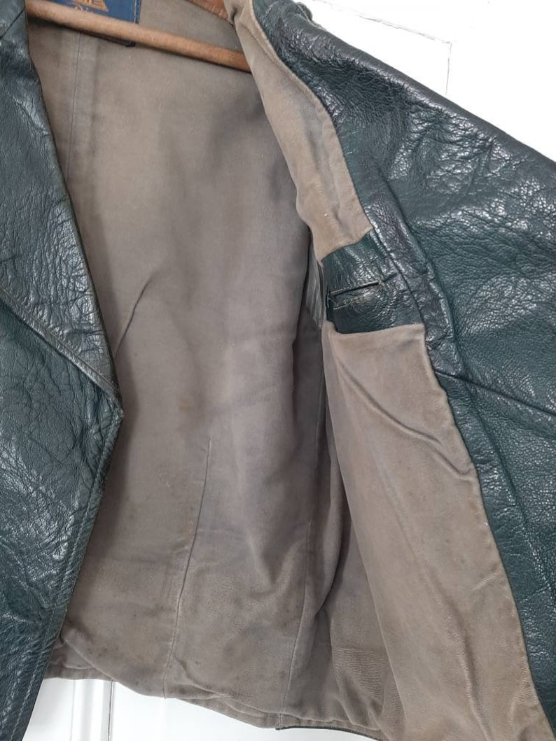 May include: A dark green leather jacket with a brown lining. The jacket is unbuttoned and the lining is visible. The jacket has a zipper closure and a collar.