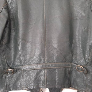 May include: A dark green leather jacket with a zipper closure and a belt at the waist. The jacket has two pockets on the front and a zippered pocket on the left sleeve.