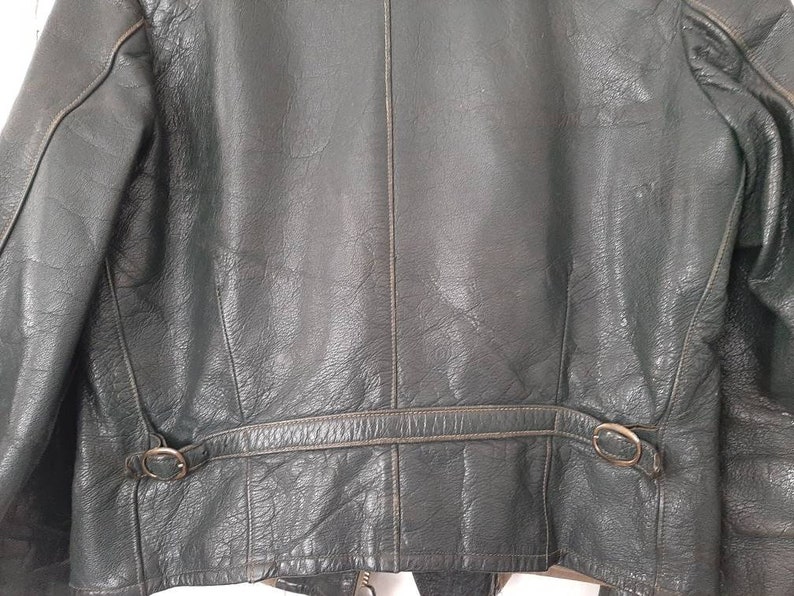May include: A dark green leather jacket with a zipper closure and a belt at the waist. The jacket has two pockets on the front and a zippered pocket on the left sleeve.