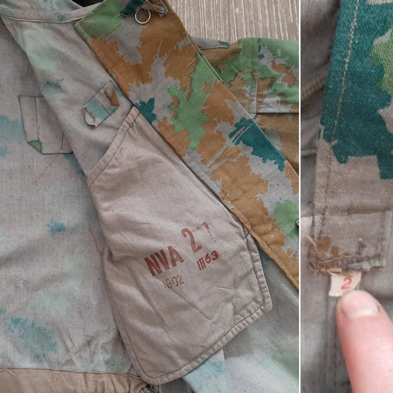 K&ouml;nnte beinhalten: Nahaufnahme einer Tarnjacke mit einer Tasche, auf der der Text "NVA 27 802 III 63" aufgedruckt ist. Die Jacke ist aus hellbraunem, gr&uuml;nem und braunem Stoff.