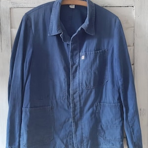May include: A blue work jacket with multiple pockets and a button closure. The jacket has a small patch on the chest with the letter "S" on it.