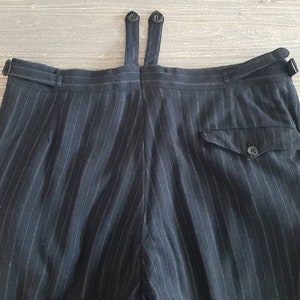 Puede incluir: Pantalón negro de rayas finas con un bolsillo trasero y un cierre de botón. El pantalón tiene un lazo para tirantes con dos botones.