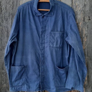 May include: A blue denim work jacket with a button-up front, two chest pockets, and two lower pockets. The jacket has a collar and long sleeves.