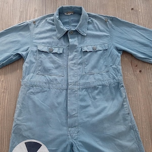 Peut inclure: Une combinaison de travail bleu clair avec deux grandes poches sur la poitrine et une fermeture éclair. La combinaison a une coupe ample et est faite d'un tissu de coton résistant.