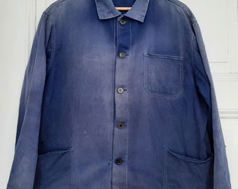 May include: A faded blue work jacket featuring a classic collar, a button-down front with five dark buttons, one chest pocket on the left side, and two large patch pockets at the bottom. The garment has long sleeves and a straight hemline.