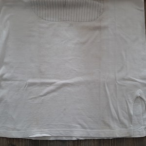 Op de afbeelding: Een wit T-shirt met een kleine split aan elke kant van de zoom. Het shirt heeft een textuurontwerp op de bovenrug.