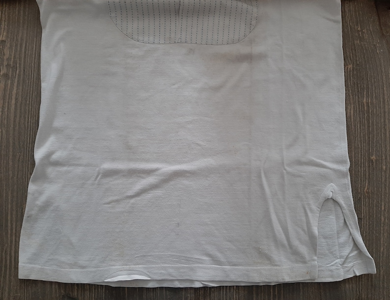 Op de afbeelding: Een wit T-shirt met een kleine split aan elke kant van de zoom. Het shirt heeft een textuurontwerp op de bovenrug.