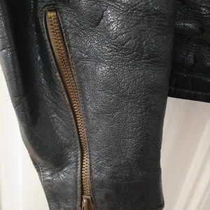 May include: Close-up of a black leather jacket with a brass zipper on the sleeve.