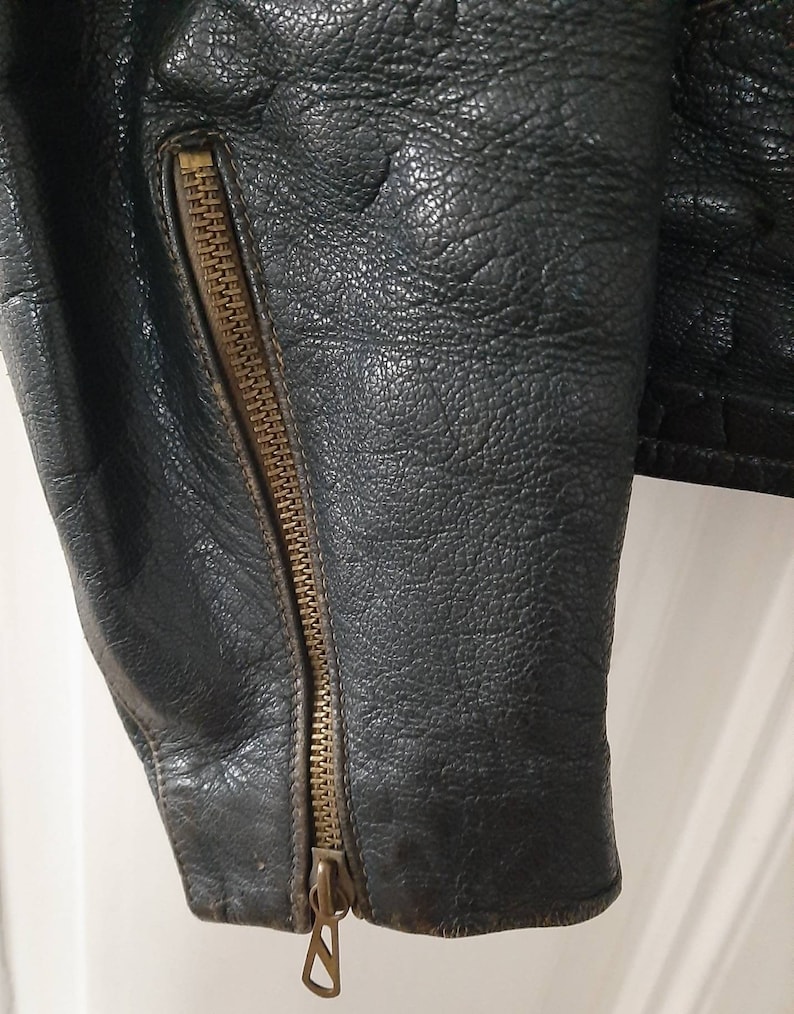 May include: Close-up of a black leather jacket with a brass zipper on the sleeve.