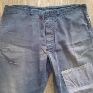 May include: A pair of blue denim pants with a patch on the right knee. The pants have a faded look and are made of a durable material.