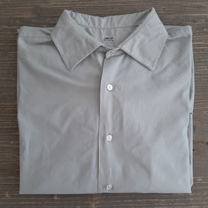 May include: A light gray long-sleeved button-down shirt with a collared neckline. The shirt has a label that reads "Sanfor."