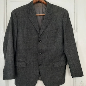 May include: A dark gray blazer with a subtle checkered pattern. The blazer has a three-button closure and two flap pockets.