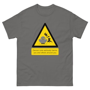 May include: A gray t-shirt with a yellow warning sign that says "Demon core seriously harms you and others around you." The sign has a black triangle with a stylized image of a sphere with lightning bolts coming out of it.