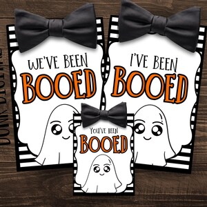May include: Halloween-themed gift tags with black bow ties. The tags feature a ghost illustration and the phrases "We've Been Booed" and "You've Been Booed" in orange and black lettering. The background is white with a black and white striped border.