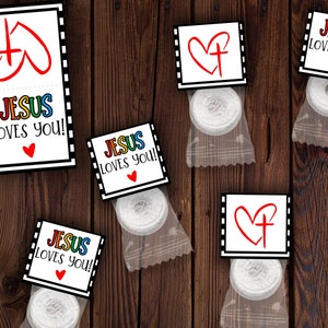 Peut inclure: Cinq petits sacs cadeaux contenant des bonbons à la menthe blanche. Chaque sac présente un design différent avec un cœur rouge et les mots "Jésus vous aime !" en lettres colorées.