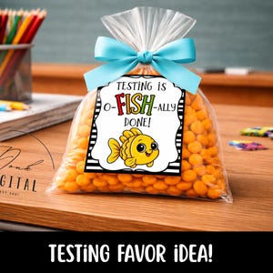 May include: A clear cellophane bag filled with orange candies, tied with a light blue ribbon. A tag reads "Testing is o-FISH-ally DONE!" with a cartoon fish illustration. The words "Testing Favor Idea!" are at the bottom.