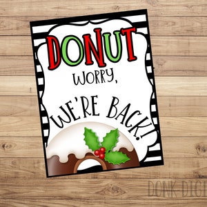 May include: A white sign with black and white stripes on the edges. The sign has a donut with green holly and red berries on top. The text on the sign reads "Donut worry, we're back!"