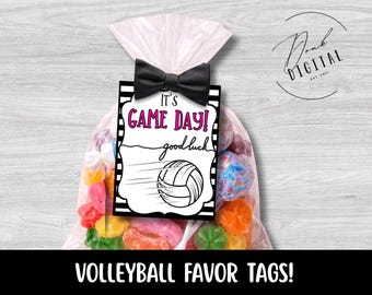 May include: A clear plastic favor bag filled with colorful candies, featuring a rectangular tag with black and white stripes, a black bow tie, and the text It's GAME DAY! good luck, accompanied by a black and white line drawing of a volleyball.