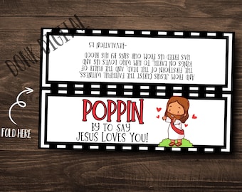 May include: A folded card with the text "POPPIN BY TO SAY JESUS LOVES YOU!" in red. The card features an illustration of Jesus and a Bible verse. The card is black and white with a wooden background.