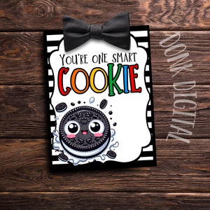 Puede incluir: Una tarjeta imprimible con una pajarita negra en la parte superior y el texto "You're one smart cookie" en letras de arcoíris. Una galleta de dibujos animados con una cara está debajo del texto.