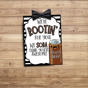 Peut inclure: Une carte ray&eacute;e noire et blanche avec un n&oelig;ud papillon en haut. La carte dit "We're Rootin' for you We Soda think you're awesome!" et pr&eacute;sente une canette de bi&egrave;re de gingembre en dessin anim&eacute; avec un visage souriant.