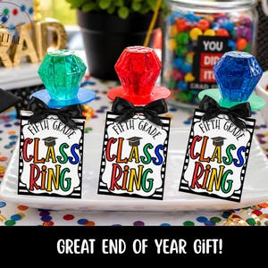 Op de afbeelding: Drie ringpops met juweelvormige snoepjes in groen, rood en blauw, elk bevestigd aan een label met de tekst "Fifth Grade Class Ring". De labels zijn versierd met een afstudeerhoed en een zwarte strik. De tekst "GREAT END OF YEAR GIFT!" staat onderaan.