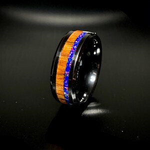 May include: A black tungsten carbide ring with a wooden inlay and a blue opal accent.