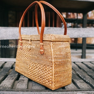 May include: A woven rattan handbag with brown leather handles. The bag has a rectangular shape and a woven pattern.