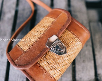 May include: A small brown leather and woven crossbody bag with a silver clasp. The bag has a woven pattern and a leather flap.