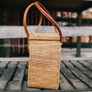May include: A brown woven rattan handbag with a brown leather strap. The bag is sitting on a wooden surface.