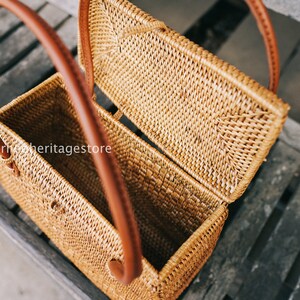 May include: A woven rattan box with a hinged lid and two brown leather handles. The box is open and the inside is visible.