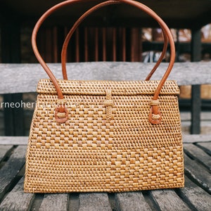 May include: A woven rattan handbag with brown leather handles and a flap closure. The bag has a rectangular shape and a woven pattern.