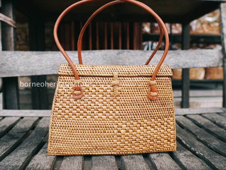 May include: A woven rattan handbag with brown leather handles and a flap closure. The bag has a rectangular shape and a woven pattern.