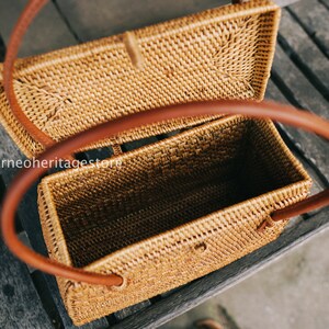 May include: A woven rattan handbag with a brown leather handle. The bag is open and the inside is visible. The bag is sitting on a wooden surface.