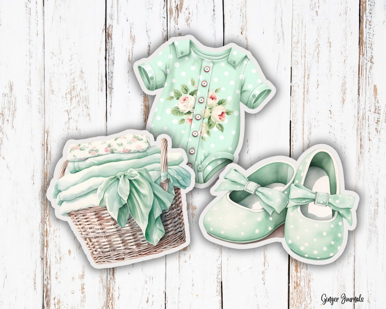 May include: Watercolor illustration of baby items: a mint green onesie with floral accents, a pair of polka-dot shoes with bows, and a wicker basket with folded blankets and a ribbon. The items are on a white wooden background.