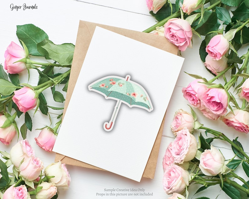 May include: A sticker of a teal umbrella with a floral pattern and polka dots. The umbrella has a red handle and is set on a white card with a brown envelope. Pink roses surround the card. The text "Ginger Journals" is in the top left corner.