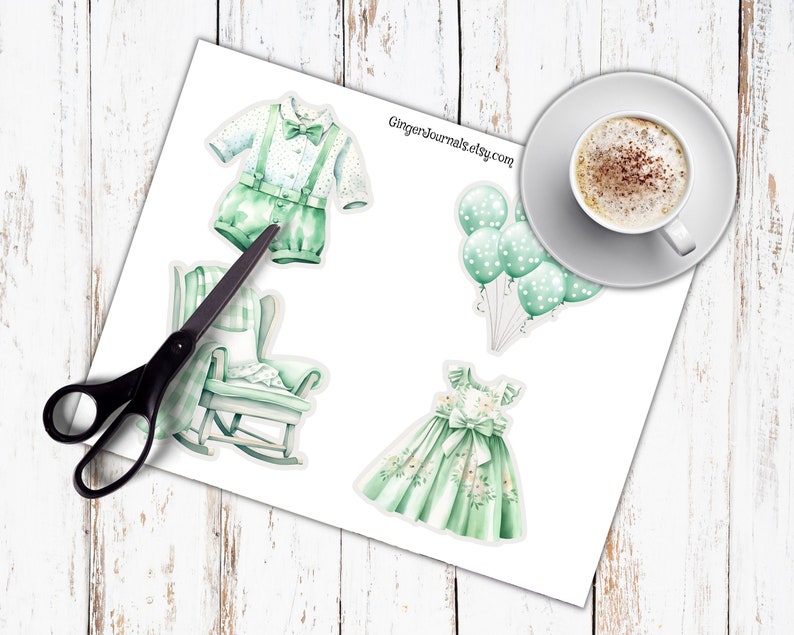 May include: Watercolor stickers of baby-themed items, including a green romper with suspenders, a rocking chair, a dress, and balloons. A cup of coffee sits on a saucer in the upper right corner. The text "GingerJournals.etsy.com" is visible.