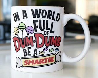 May include: White ceramic mug with a black and red graphic that says "In a world full of Dum-Dums be a Smartie". The graphic includes colorful lollipops and candy.