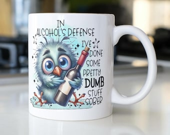 May include: White ceramic mug with a blue bird illustration holding a bottle of wine. The mug has the text "In alcohol's defense I've done some pretty dumb stuff sober."