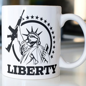 May include: White ceramic mug with a black and white image of the Statue of Liberty holding a rifle. The image is surrounded by a circle of stars and the word "LIBERTY" is printed below the image.