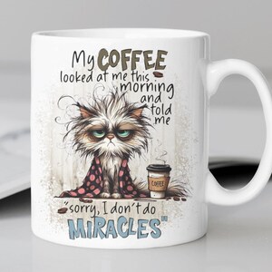 May include: White ceramic coffee mug with a cartoon illustration of a grumpy cat with a cup of coffee. The text on the mug reads "My coffee looked at me this morning and told me "sorry, I don't do miracles".